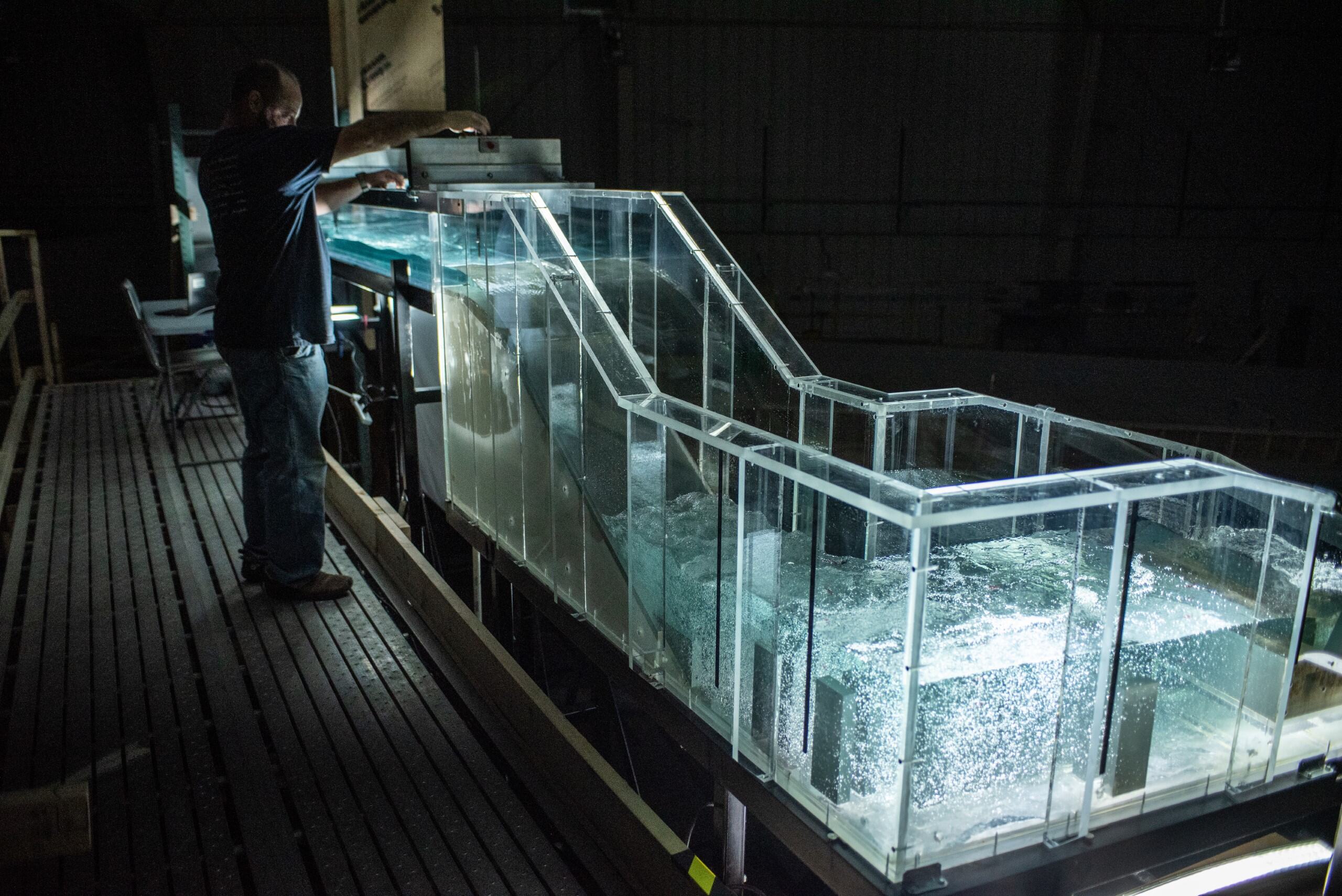 An IIHR workers works on an aspect of a modeled water system, lit up from underneath, in a dark warehouse
