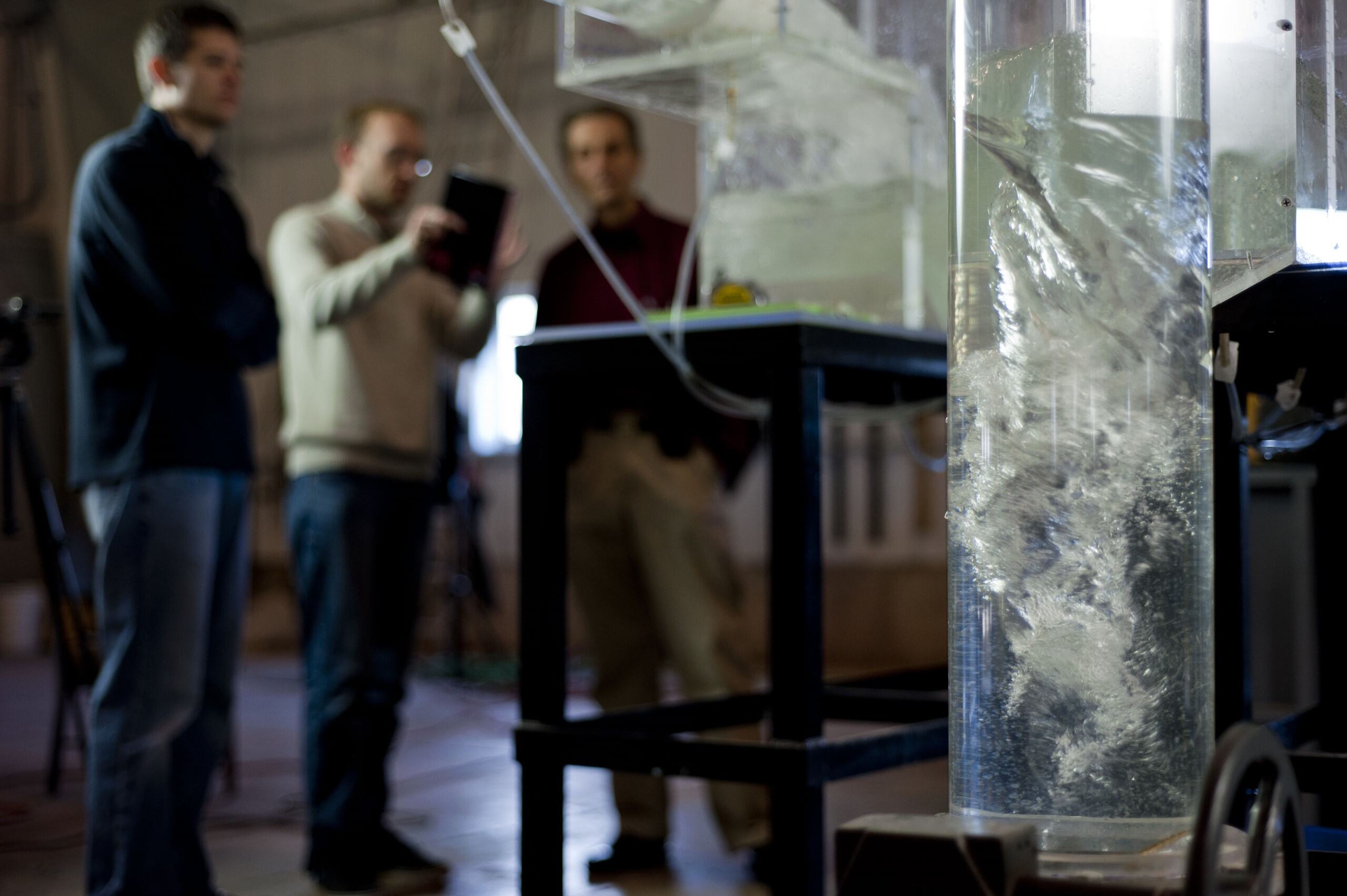 IIHR workers discuss work in the background, as the model in view showcases a whirlpool effect inside a vertical tube