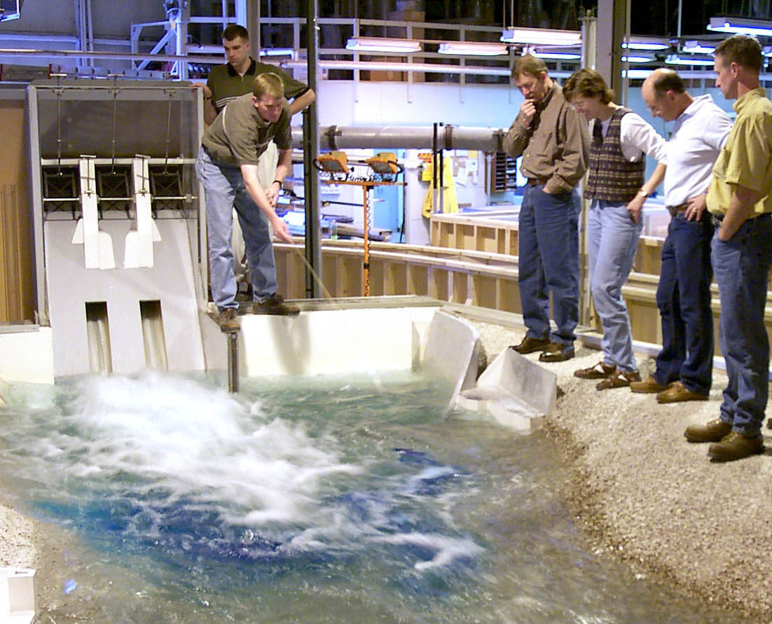 The model of Hells canyon dam inside IIHR's facility, with a group gathered around looking at the spillway section as water flows through