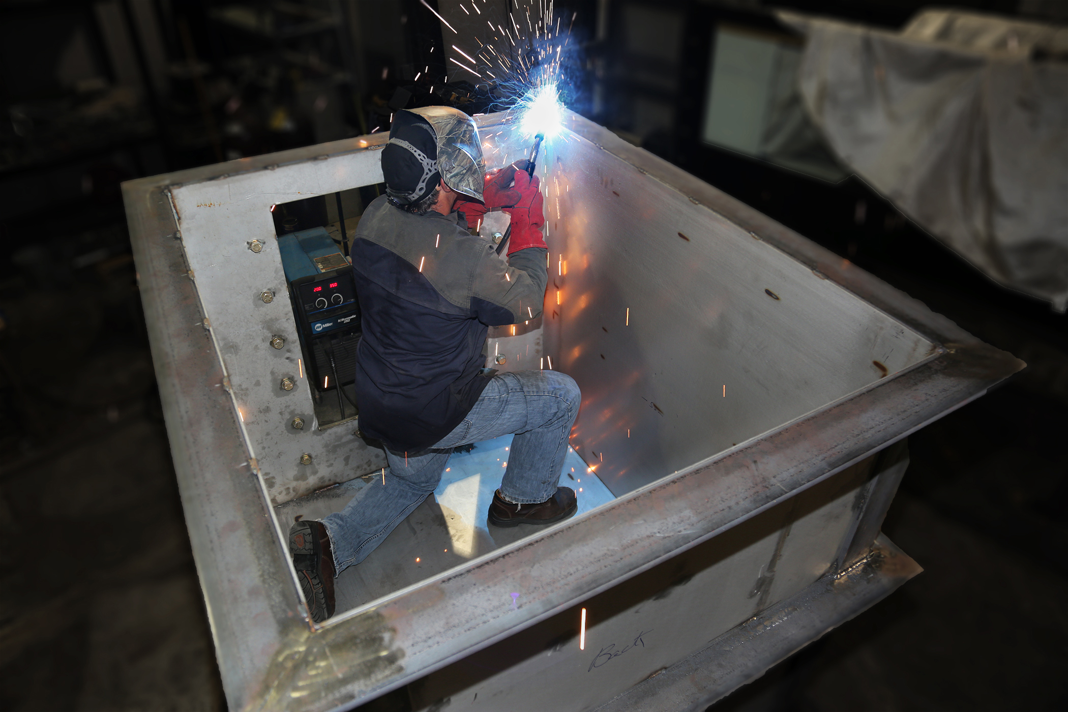 An IIHR worker works inside a metal box, welding one of the sides