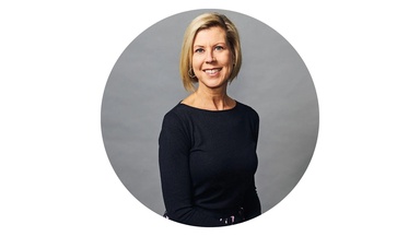Sharon Krause smiles, sitting on a chair