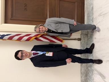 A tall man and a short woman pose in front of an American flag