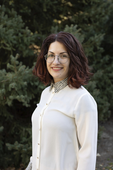 A smiling woman poses in front of some greenery