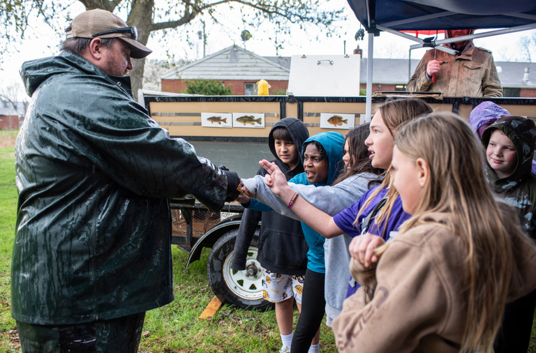 DNR workers handle a fish, showing it to a group of kids
