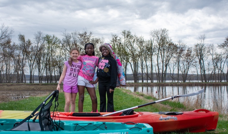 Kids pose in front of a kayak
