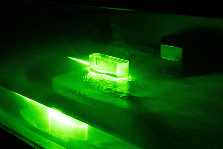 A model of a bridge pier glowing green in the experimental flume with water slowing around it