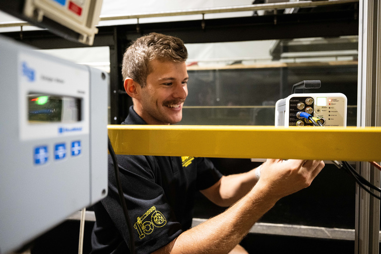 An IIHR student researcher smiles and makes adjustments to the equipment in the flume