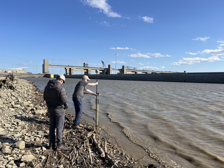 Two researchers work on getting measurements on the side of the Mississippi River