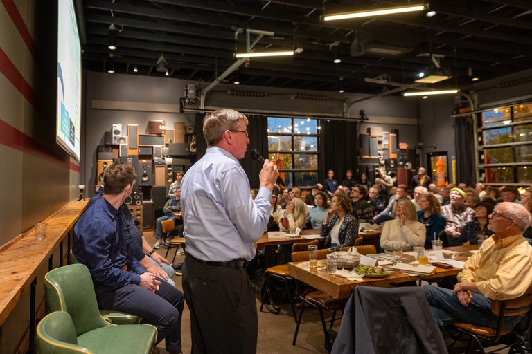 IIHR Director Larry Weber stands on the panel, holding the microphone and addressing the large crowd