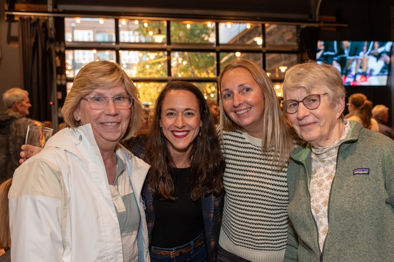 a group of IIHR workers and partners smile, the sun setting behind them through the window