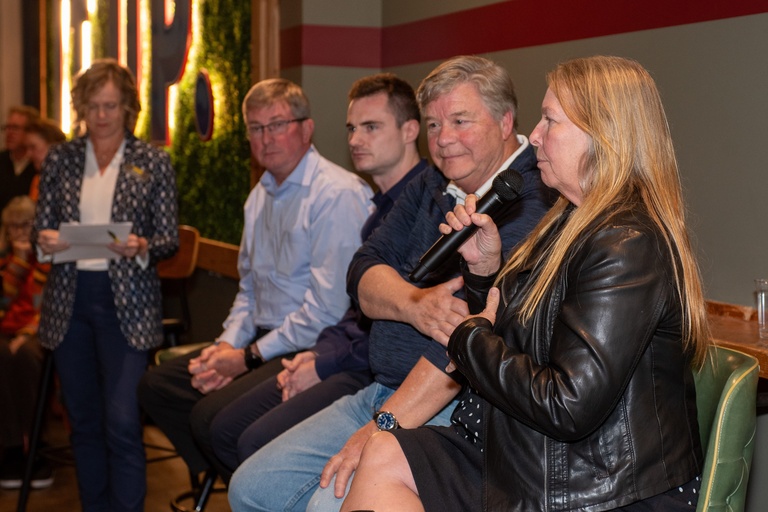 Mary Skopec addresses the crowd with the microphone while sitting on a green leather chair