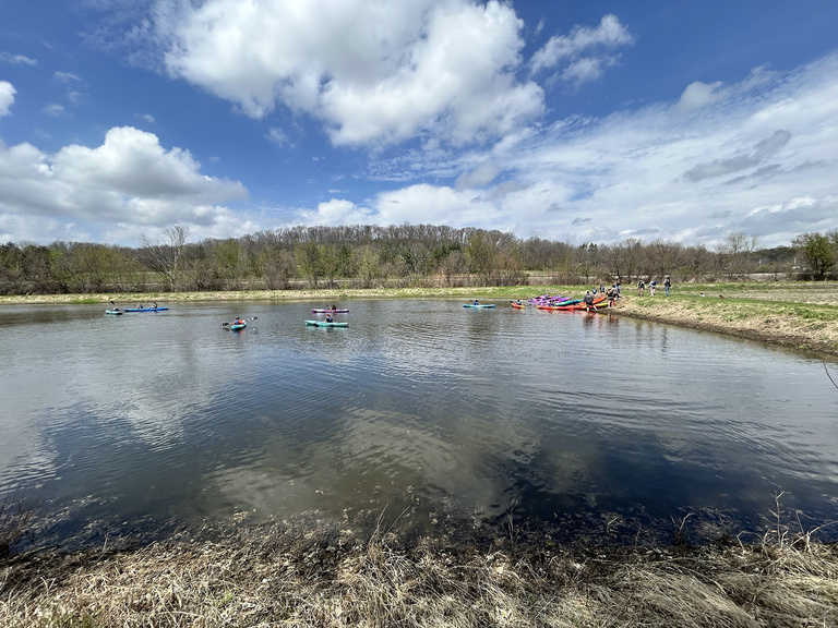 Students in colorful kayaks paddle around a pond