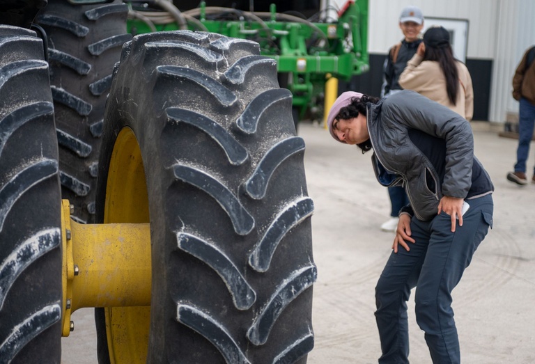 A woman leans over sideways to read the words on a gigantic black tractor tire