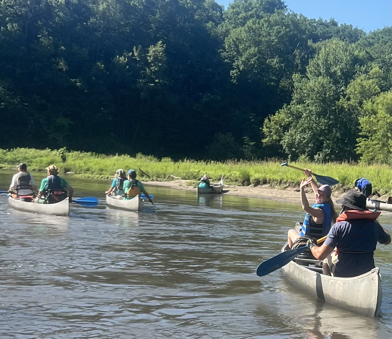 A young woman waves from her canoe as other canoes float by