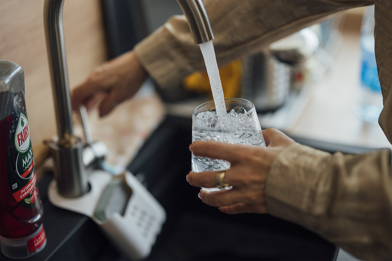 Closeup of water flowing out of a faucet into a glass held by a man
