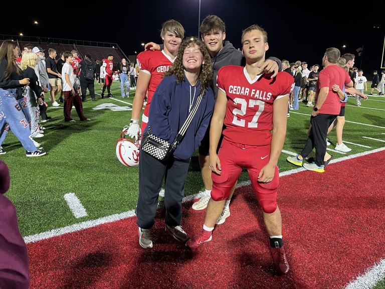 A smiling family gathers on the sidelines of a football game. Two people are in a red football uniform.