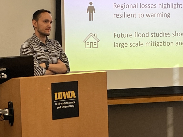 A young man stands at a podium with a project screen behind him