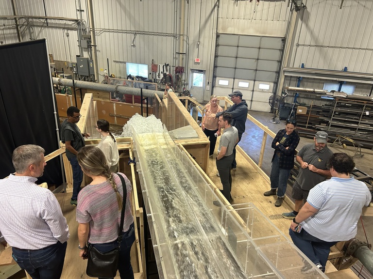 A group of people look at water flowing through a hydraulic structure model