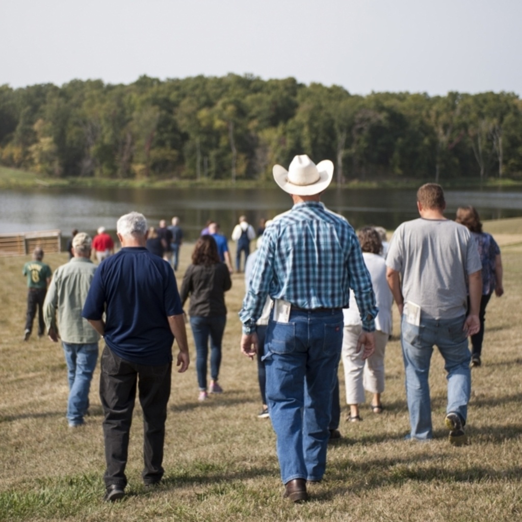 A group of people walking away from the camera toward a lovely farm pond.