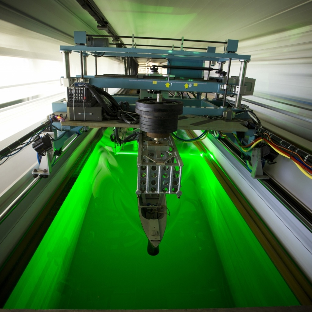 Laser colors the water of the tow tank bright green as the platform with attached ship model moves through the water