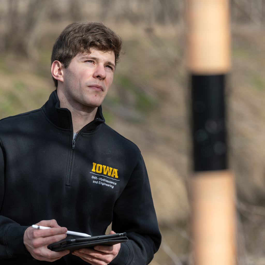 Graduate student Anthony Lamoreux looks out at a creek, holding a piece of equipment