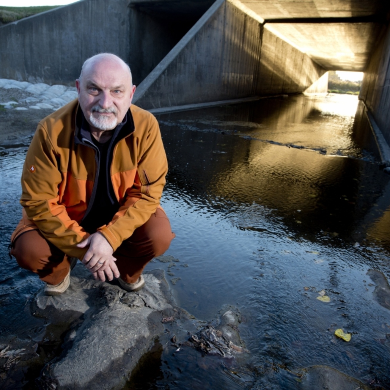 A researcher kneels in a culvert with water flowing by his feet.