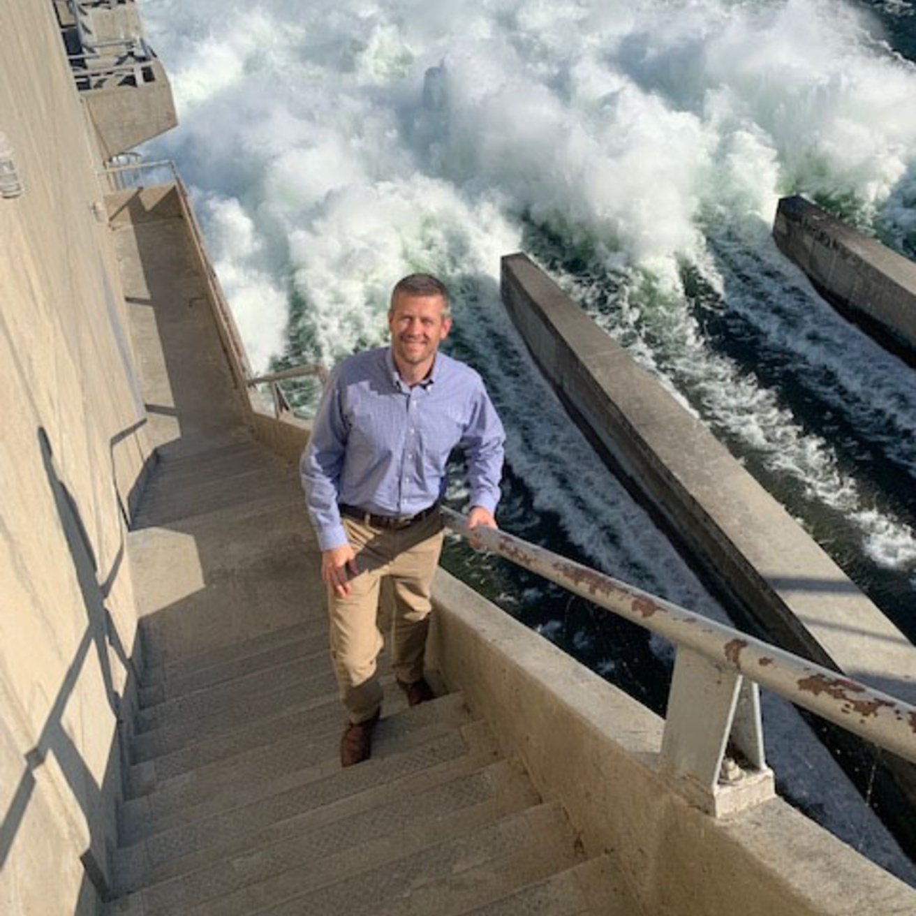 Troy Lyons stand on the stairs of a Dam, with the water surging below him