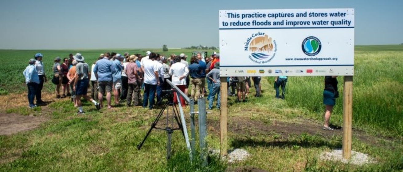 A group of people standing behind a sign identifying a constructed wetland