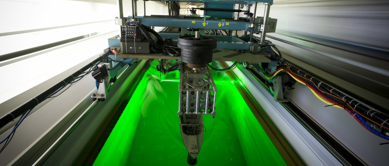 Laser colors the water of the tow tank bright green as the platform with attached ship model moves through the water