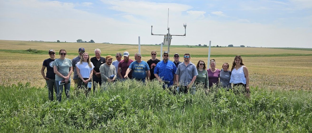A watershed group poses for a picture in a cornfield, with the IFC hydrostation behind