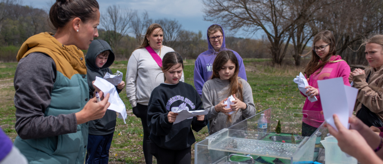 Breanna Shea discusses the watershed model with children surrounding