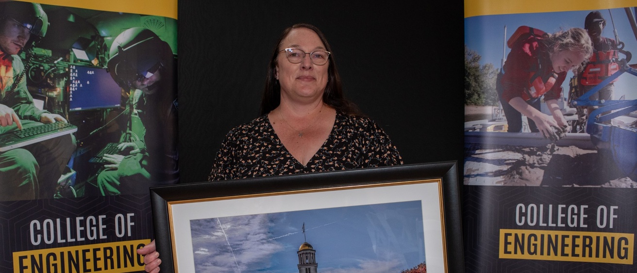 Teresa Gaffey smiles, holding a painting of the Old Capital building while being honored