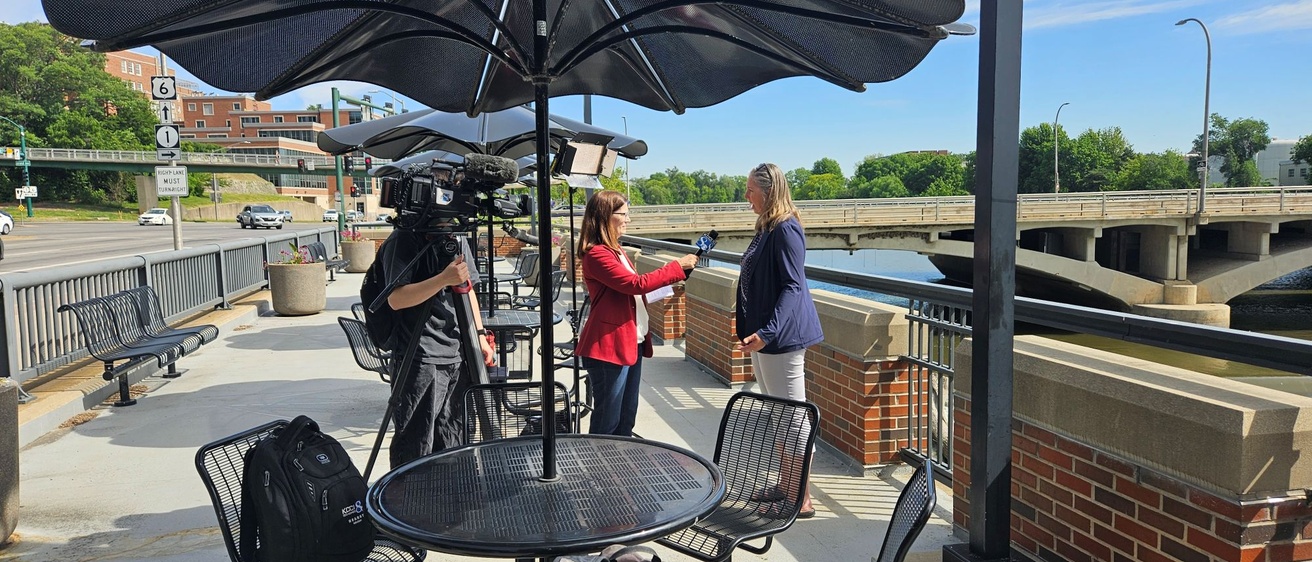 A woman reporter holds a microphone to interview another woman in a blue blazer on the terrace of Stanley Hydraulic Lab