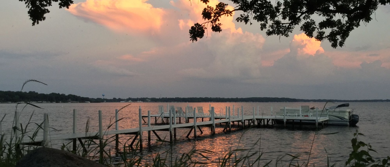 Colorful clouds at sunset reflect on the waters of West Lake Okoboji with a dock in the foreground