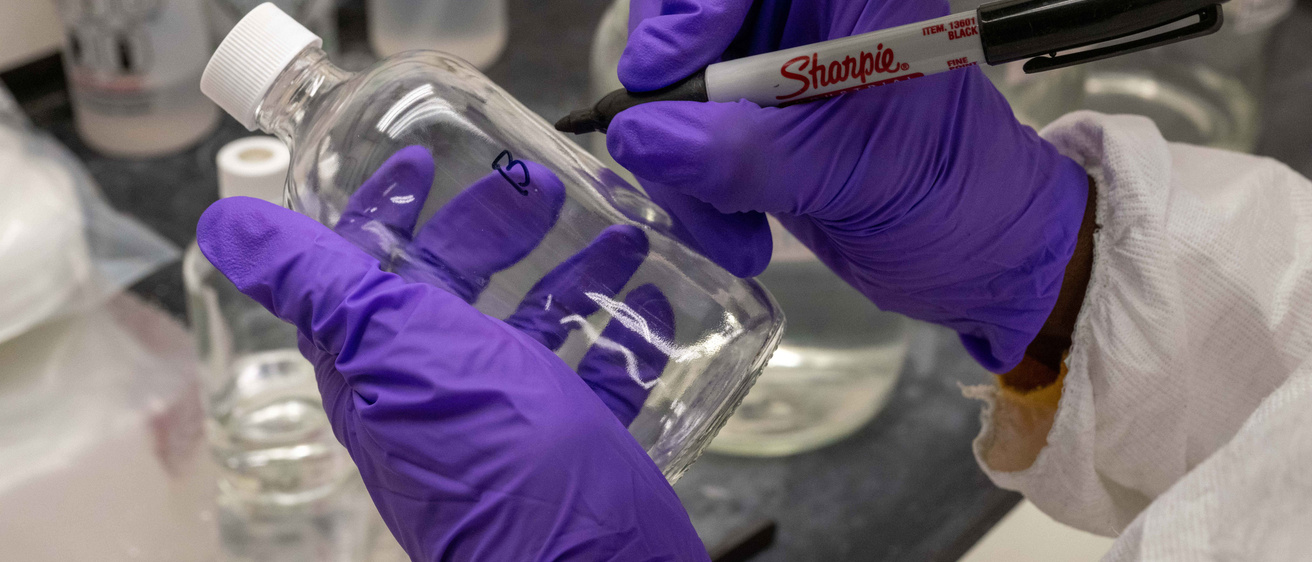 person writing on a glass bottle in a lab