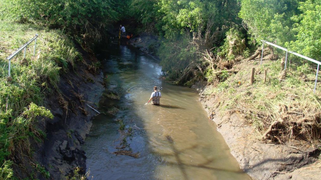 A man in waders in a brown-water creek