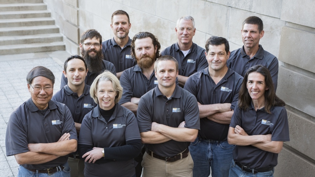 A group of smiling men and women stands with arms crossed.