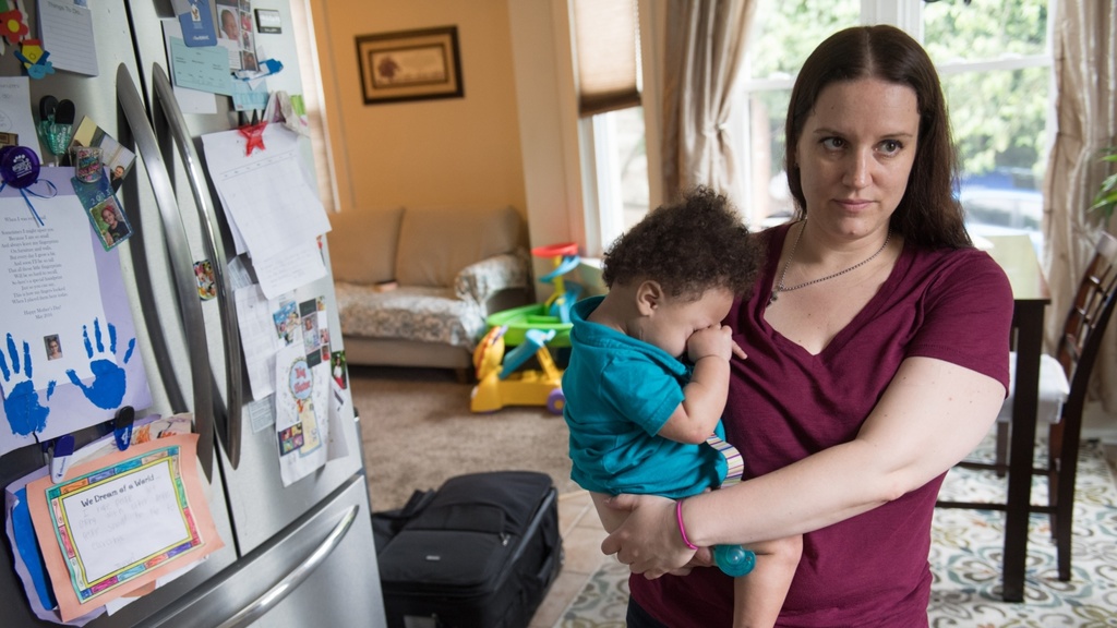 A woman holds a small child on her hip while standing in the kitchen of her home.