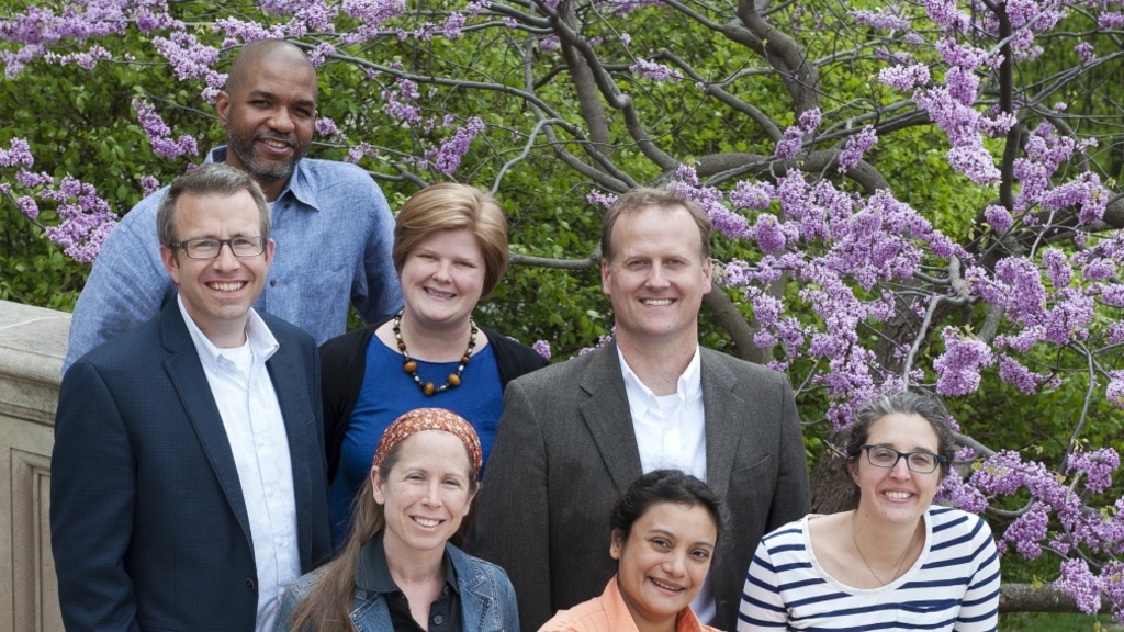 A group of men and women poses in front of a blooming tree