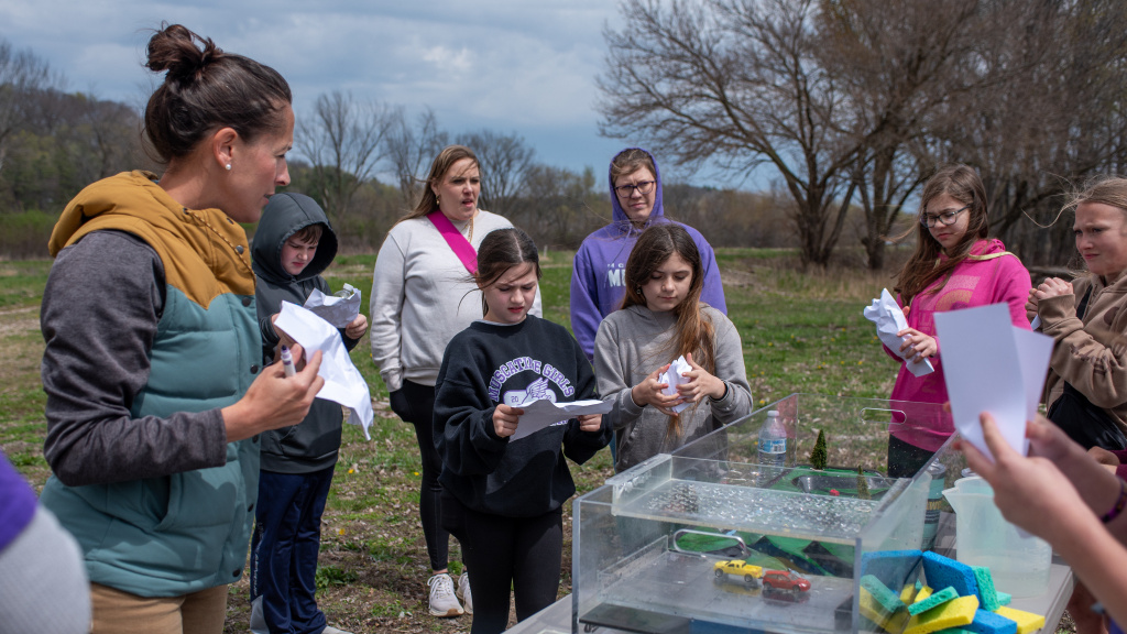 Breanna Shea discusses the watershed model with children surrounding