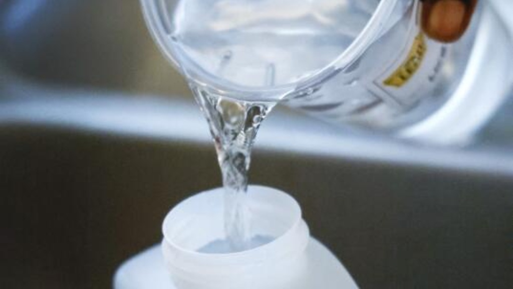 a woman pouring a cup of water into a plastic bottle for testing