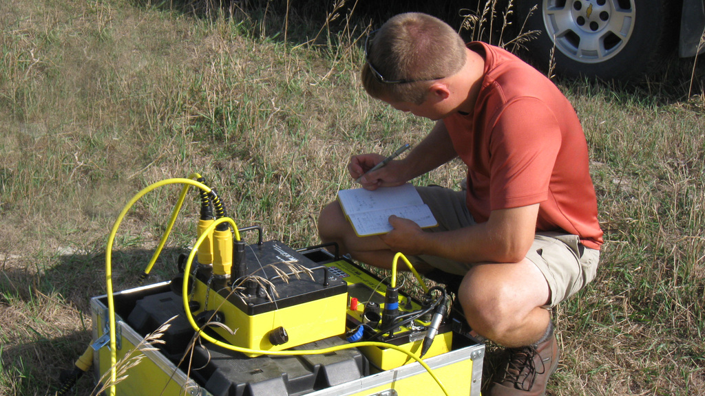 IGS worker checks groundwater levels with a large piece of equipment and takes notes