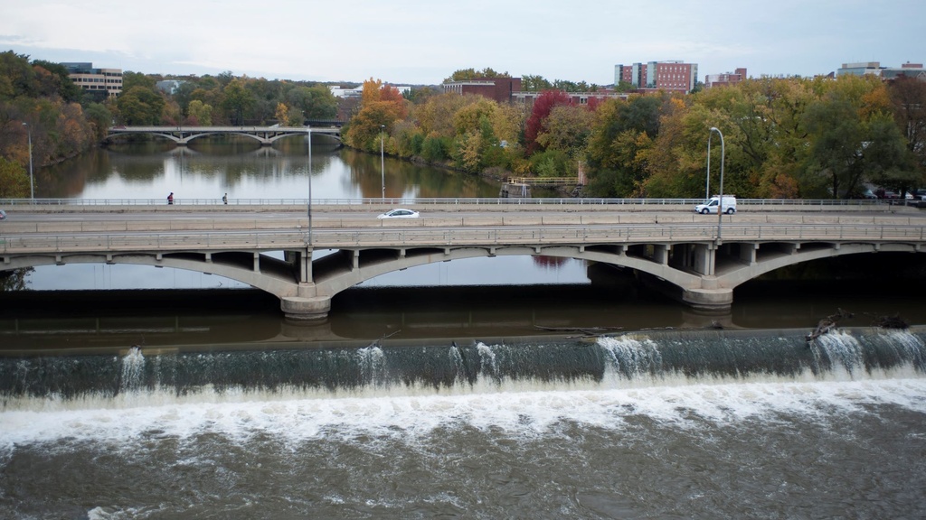 The Iowa River flowing over a small dam as it passes by the University of Iowa campus, with colorful fall trees on the banks.