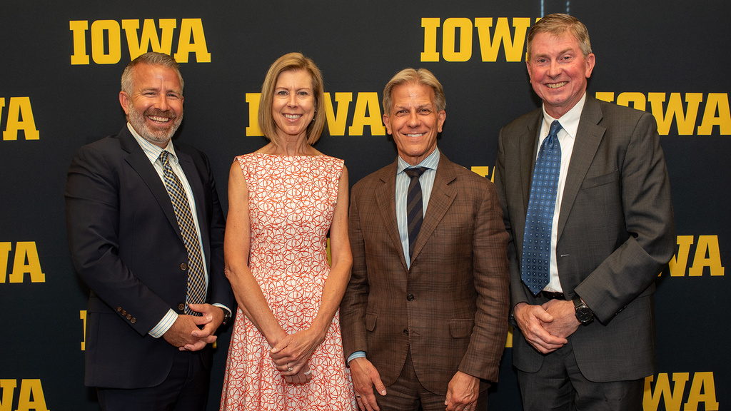 Four smiling people stand in front of a black and gold IOWA banner 