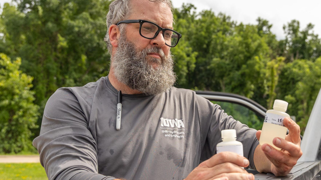 A researcher examines water quality samples with green trees behind him