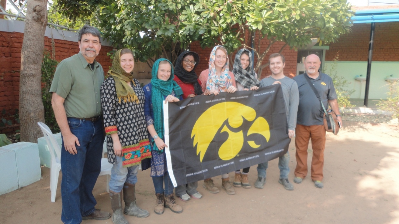 Two faculty members and a group of students in India hold a Hawkeye flag